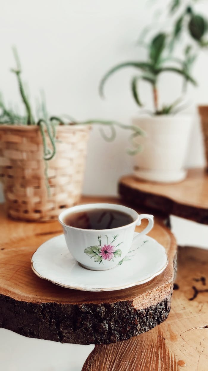 services-04 A floral porcelain cup of steaming coffee sitting on a rustic wood table with houseplants.